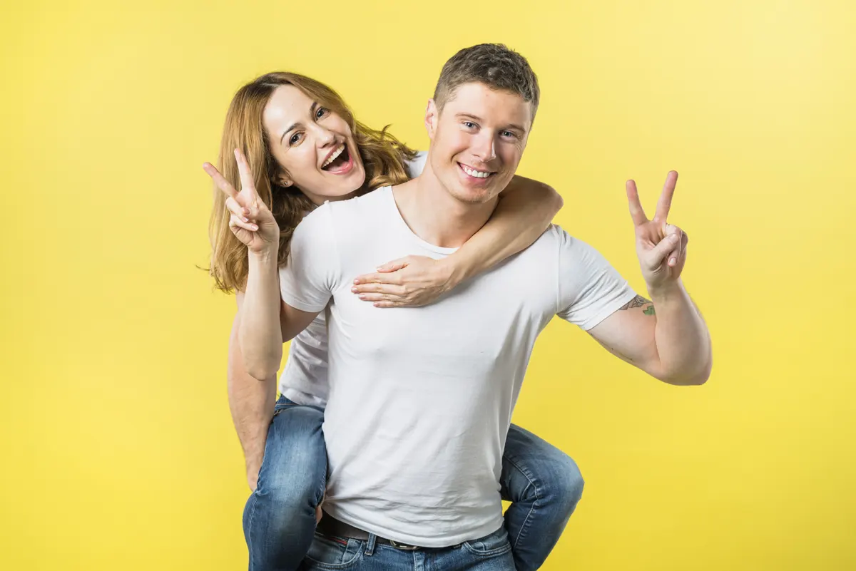 Smiling man carrying wife piggyback ride making victory sign